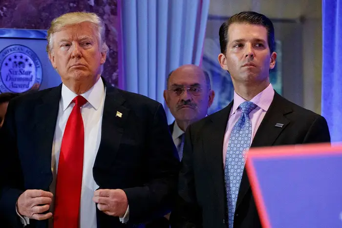 Allen Weisselberg, who is bald with a mustache and wears glasses, stands behind Donald Trump and Donald Trump Jr.